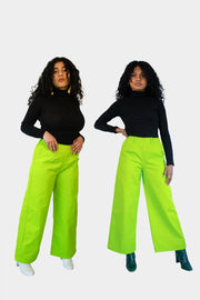 Front view of Aisha (left) and Haydon (right) wearing the Dolores Pantacourt in lime green. Cotton twill wide-legged pants with elastic waistband and invisible zipper, with pockets and belt rings. 100% Brazilian grown BCI cotton. Ethically produced in downtown São Paulo, Brazil.