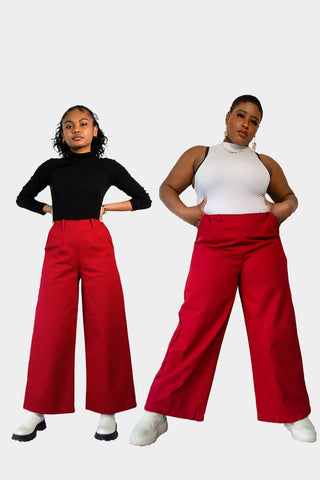 Front view of Haydon (left) and Arianne (right) wearing the Dolores Pantacourt in red. Cotton twill wide-legged pants with elastic waistband and invisible zipper, with pockets and belt rings. 100% Brazilian grown BCI cotton. Ethically produced in downtown São Paulo, Brazil